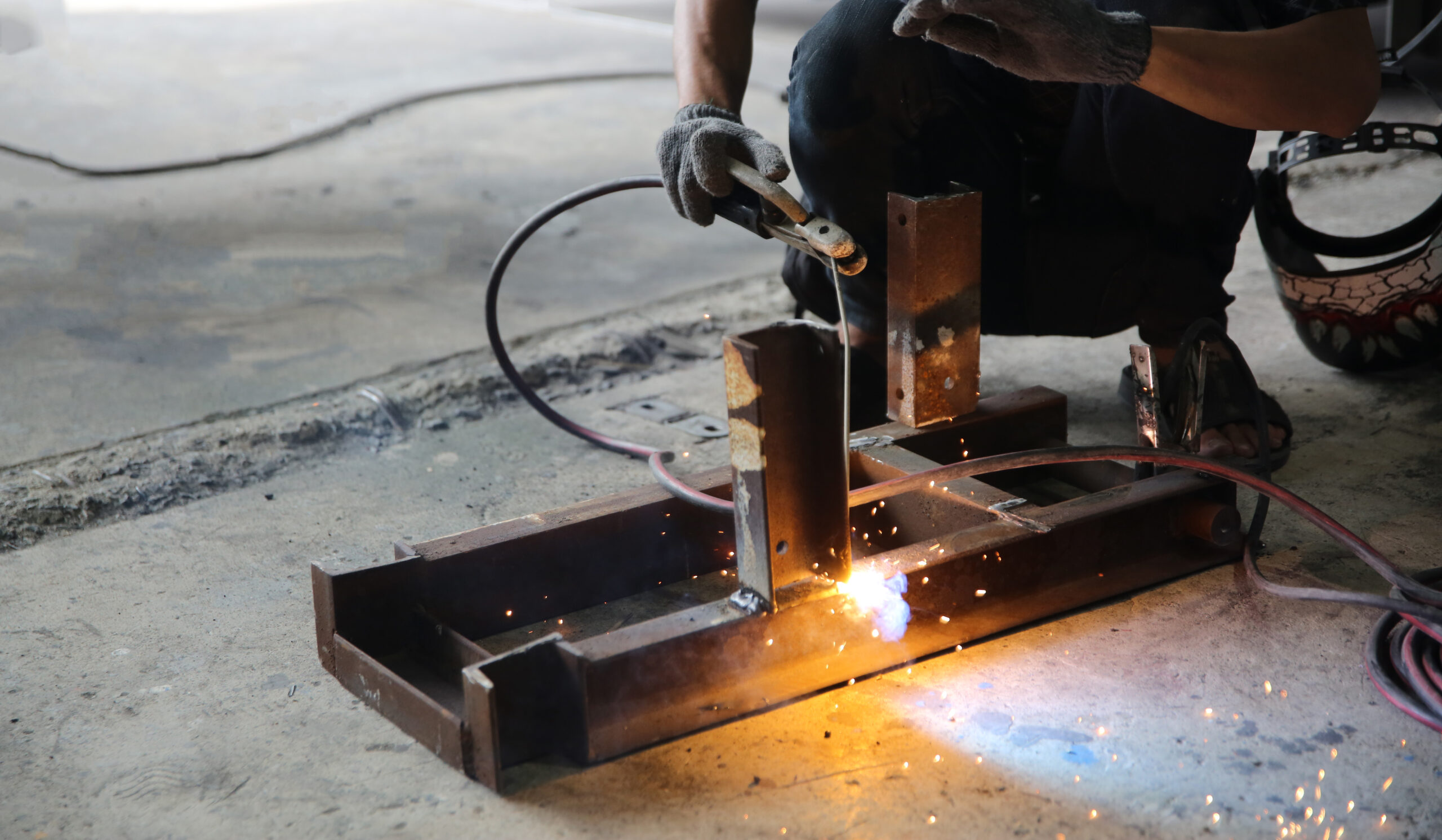 welder grinding and fabricating steel component in workshop environment