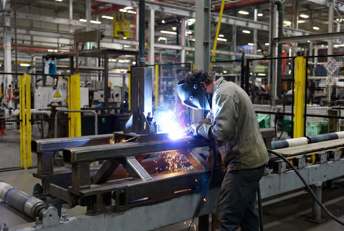 Welder working on a heavy steel fabrication jig inside a large manufacturing facility
